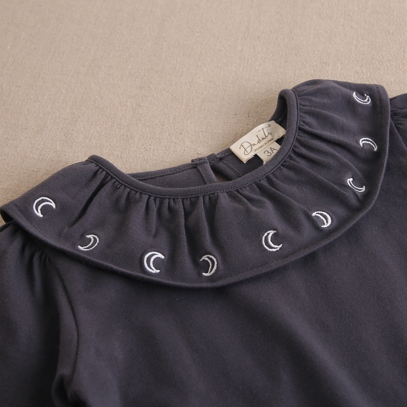 Imagen de Camiseta de niña gris oscuro con cuello volante y bordado lunas