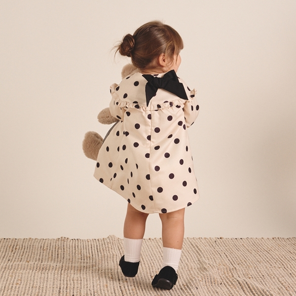 Imagen de Conjunto de bebé niña de vestido color crudo de lunares negro con lazo y calcetines blancos con pompón y abrigo acolchado camel